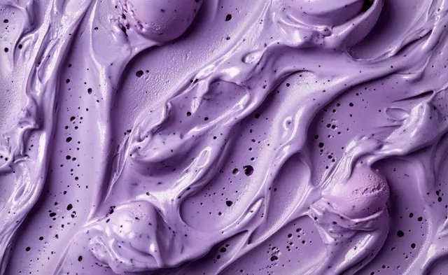 Close-up of smooth, textured purple ice cream or mousse with dark specks and swirled scoops.